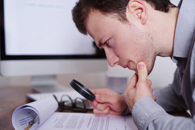 Man thoughtfully looking at documents with magnifying glass