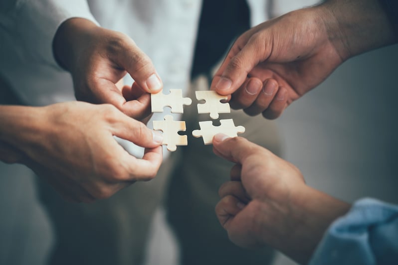 Four hands holding puzzle pieces that fit together