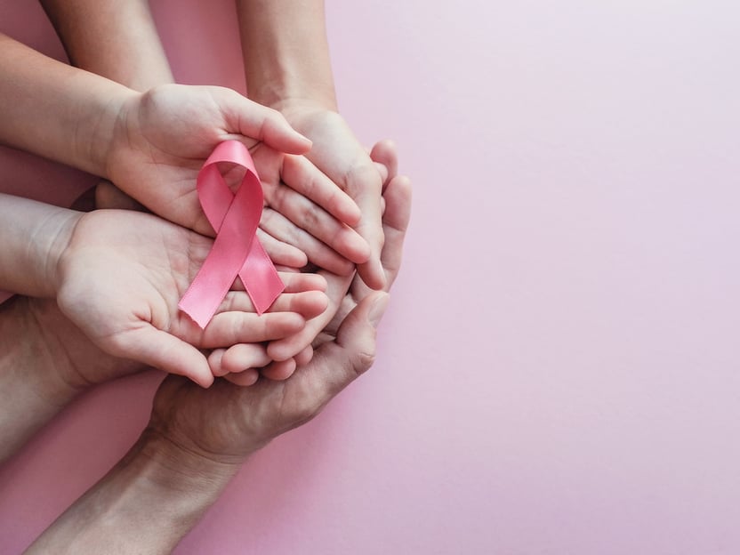 Open hands holding a pink ribbon, the symbol for breast cancer